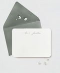White card with 'Alex & Jonathan' note card with green envelope with small white flowers on a light gray background