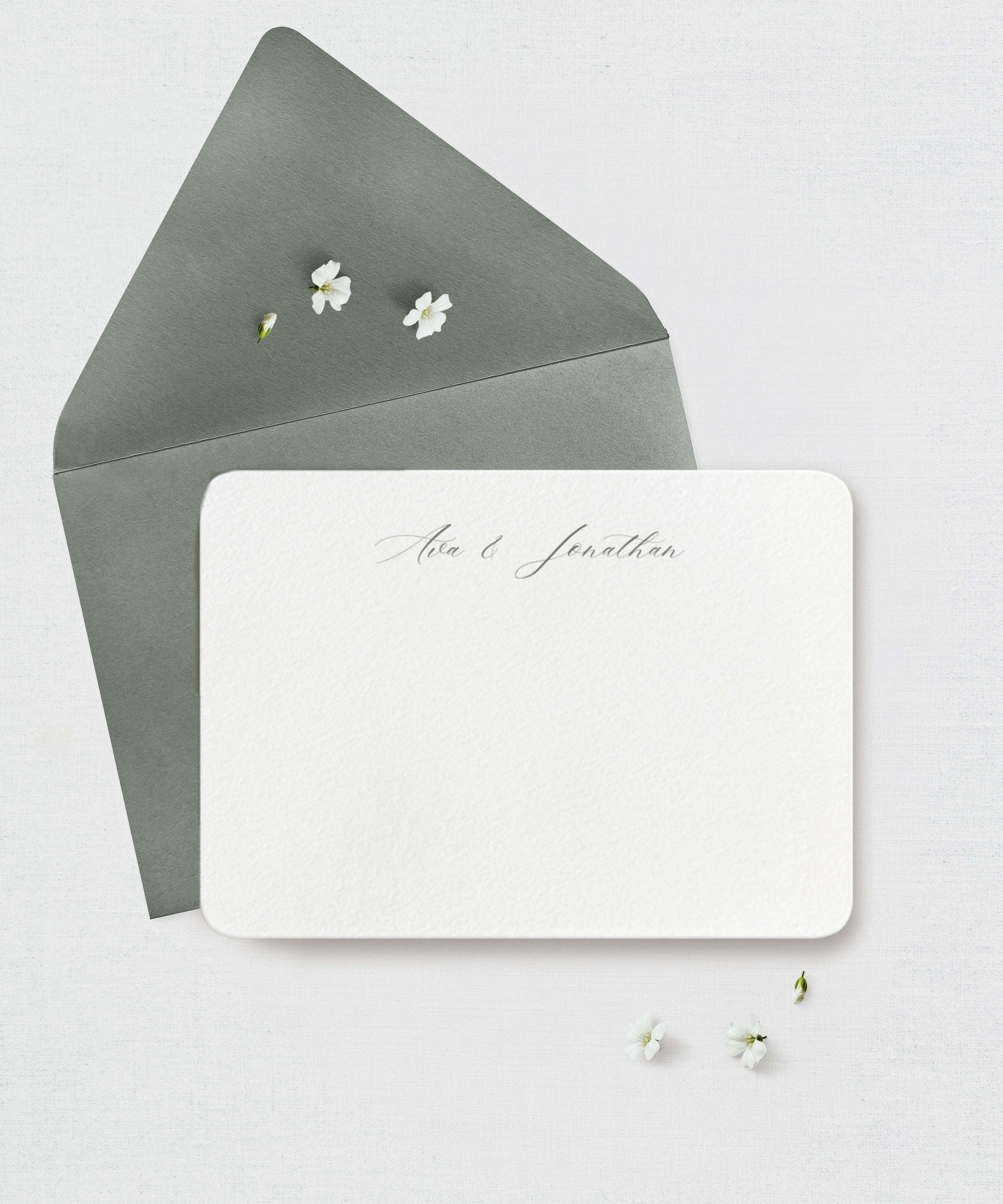 White card with 'Alex & Jonathan' note card with green envelope with small white flowers on a light gray background