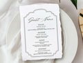 Table setting with a menu card on a white plate, accompanied by flowers and cutlery.