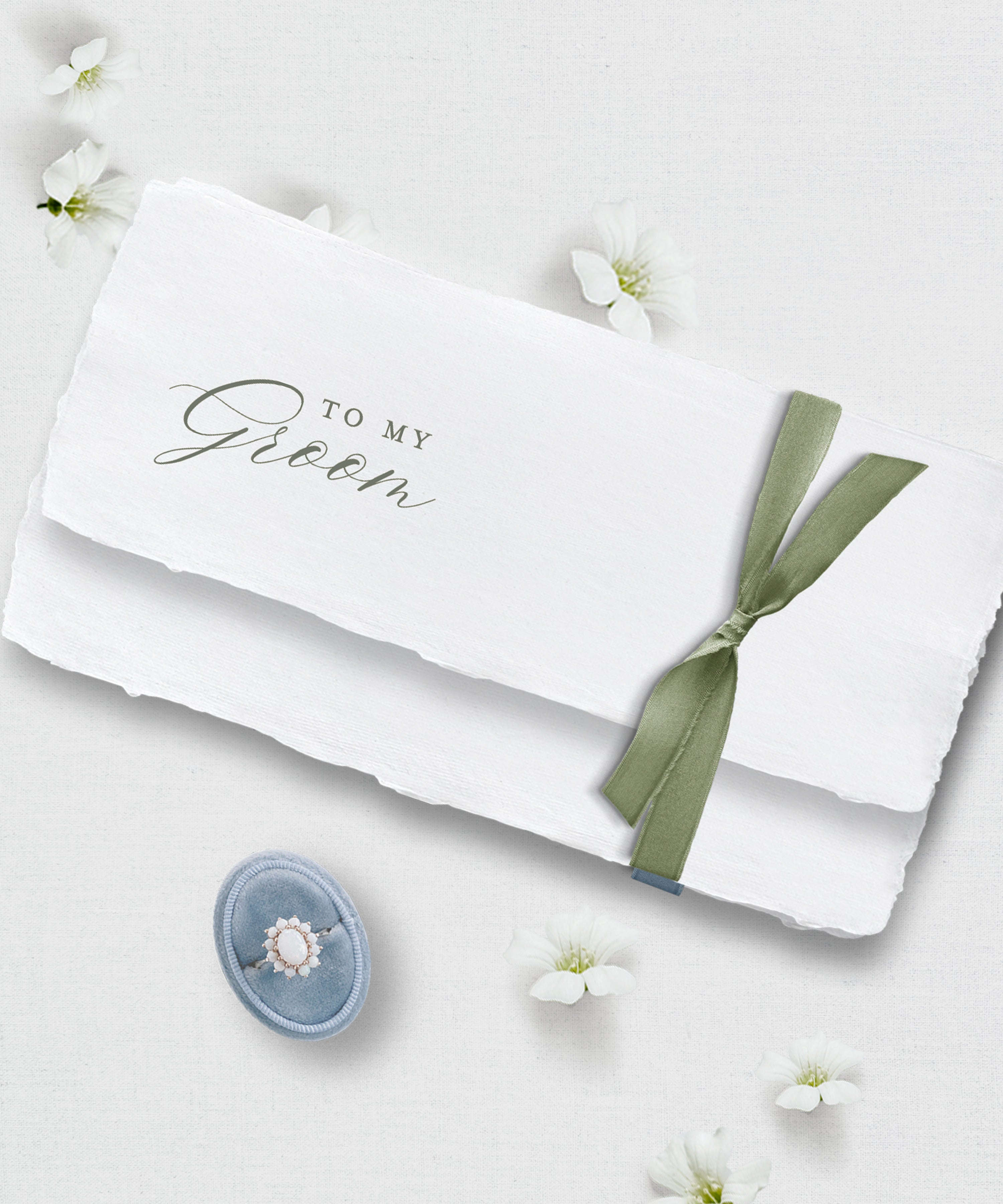 White handmade paper with 'To My Groom' text and a green ribbon on a light background with flowers.