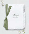 White paper with 'Vows' and a date, tied with a green ribbon on a light gray background.