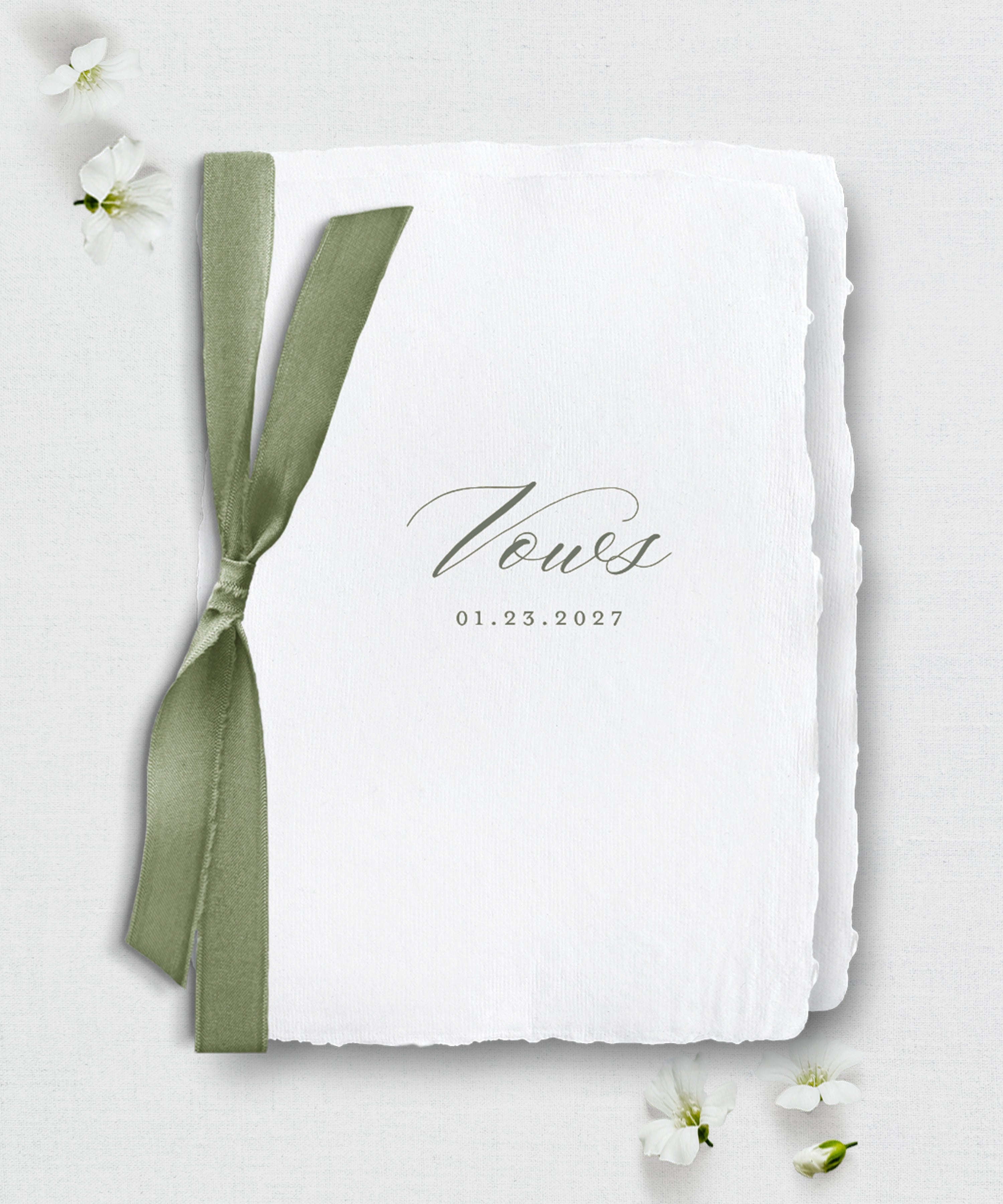 White paper with 'Vows' and a date, tied with a green ribbon on a light gray background.